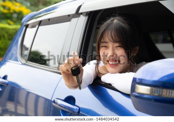Young happy Asian car driver woman\
smiling and showing new car keys. Novice drivers\
concept