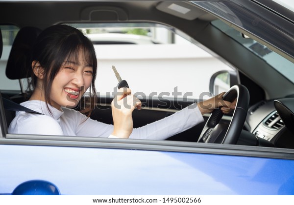 Young happy Asian car driver woman\
smiling and showing new car keys. Novice drivers\
concept