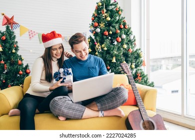 Young happy Asian couple sitting together video call on a laptop with friends or parents thanks for a gift received during the Christmas holiday with a decorated Christmas tree in the background. - Powered by Shutterstock