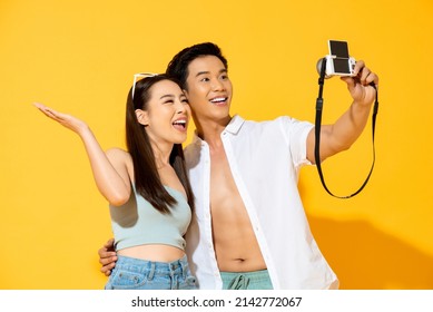 Young Happy Asian Couple Wearing Summer Outfit Taking Selfie With Camera In Studio Isolated Yellow Color Background