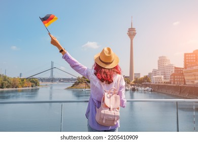 A young happy Asian girl with a German flag poses at the Media Harbor and TV-tower in Dusseldorf. Studying language abroad and traveling concept