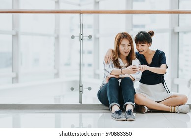 Young Happy Asian Girls Best Friends Laugh And Smile While Having Fun With Smart Phone Mobile Indoor.