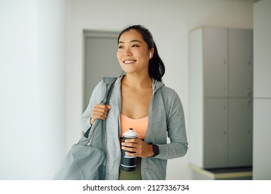 Young happy Asian sportswoman standing in locker room at the gym and looking away. - Powered by Shutterstock