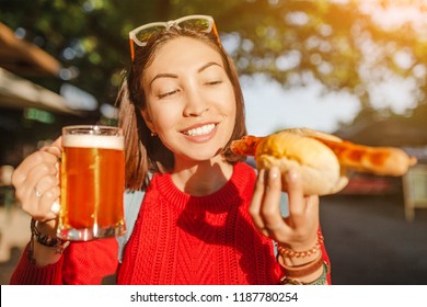 Young Happy Asian Traveler Woman Drinks Mug Of Beer With Hotdog In Germany, Beer And Food Festival Concept