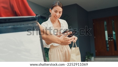 Young happy Asian woman accept paper bag from delivery man with bicycle in red uniform carry case box scan QR code payment on smartphone in front of house. express food delivery concept.