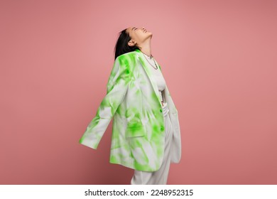 young and happy asian woman in green and white oversize blazer posing with raised head isolated on pink - Powered by Shutterstock