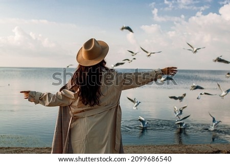 Young happy asian woman with hands in the air walks on the seaside in autumn. Seagulls flying on the beach.