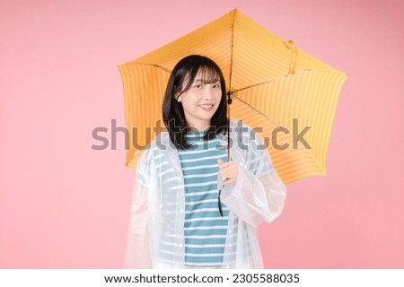 Young happy Asian woman holding yellow umbrella isolated on pink background