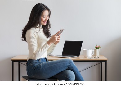 年輕快樂的亞洲女人使用智能手機在辦公室。