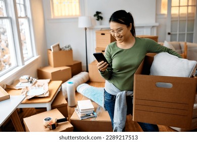 Young happy Asian woman using mart phone while unpacking her belongings in a new home. - Powered by Shutterstock