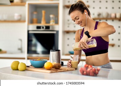 Young happy athletic woman having a fruit smoothie for breakfast in the kitchen.  - Powered by Shutterstock