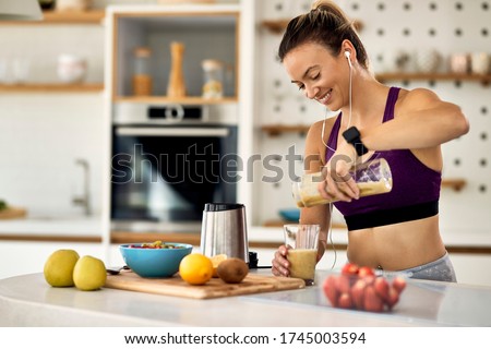 Young happy athletic woman having a fruit smoothie for breakfast in the kitchen. 
