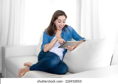 Young Happy Attractive Hispanic Woman Sitting On Living Room Sofa Couch At Home Enjoying Using Digital Tablet Computer On Wireless And Internet Leisure And Work Concept