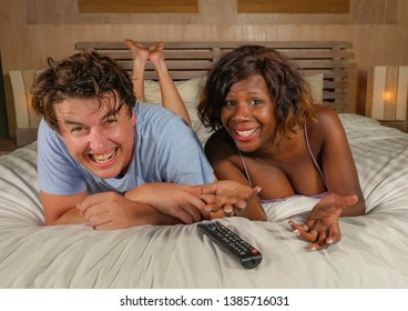 Young Happy And Attractive Mixed Ethnicity Couple With Beautiful Black Afro American Woman And Cheerful White Man At Home Lying On Bed Watching Tv Show Or Comedy Movie Laughing Together 