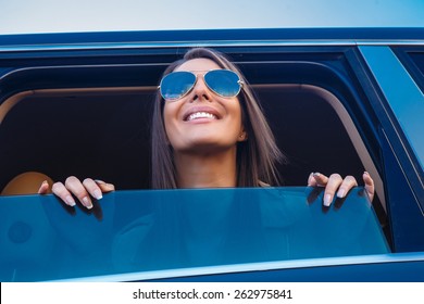 Young Happy Awesome Woman In Sunglasses Looking From A Car