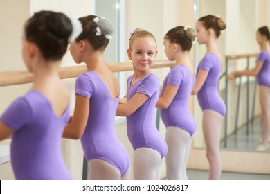 Young happy ballerina near ballet barre. Cute little ballet dancers practicing some dance element at a barre in a dance class. Professional school of ballet dance for kids.