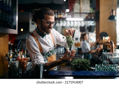 Young happy barmen preparing mojito cocktail and adding mint leaf in a glass at bar counter.