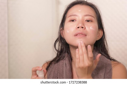 young happy and beautiful Asian Chinese woman applying moisturizer facial cream and beauty treatment at home bathroom in morning routine smiling cheerful and fresh