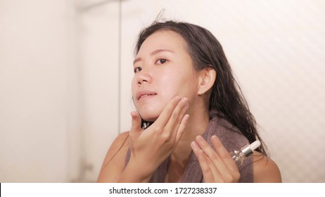 young happy and beautiful Asian Korean woman applying moisturizer facial cream and beauty treatment at home bathroom in morning routine smiling cheerful and fresh