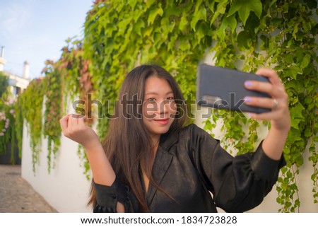 young happy and beautiful Asian Korean woman enjoying outdoors taking selfie with mobile phone at village garden playful and carefree in beauty fashion and freedom concept