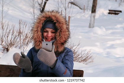 Young Happy Beautiful Woman Call Video Chatting In Winter Park In The City In Snowy Day With Falling Snow.