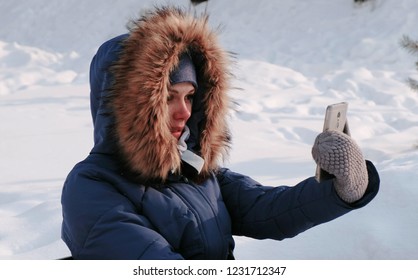 Young Happy Beautiful Woman Call Video Chatting In Winter Park In The City In Snowy Day With Falling Snow. Side View.