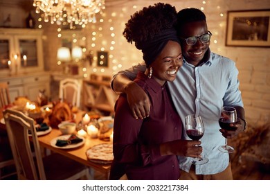 Young Happy Black Couple Embracing And Enjoying In Glass Of Wine On Thanksgiving In Dining Room.