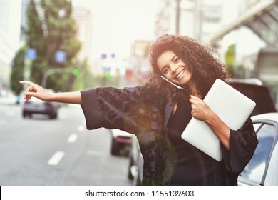 Young happy black girl try to take a taxi on the street holding a laptop