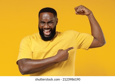 Young happy black man 20s wearing bright casual t-shirt point finger on biceps muscles on hand demonstrating strength power isolated on plain yellow color background studio. People lifestyle concept