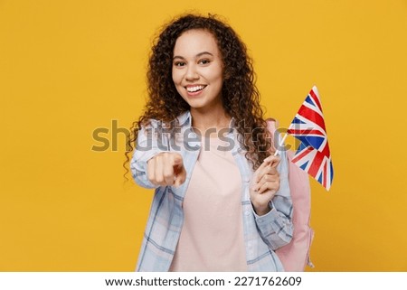 Young happy black teen girl student she wear casual clothes backpack bag hold british flag point finger camera on you isolated on plain yellow color background. High school university college concept