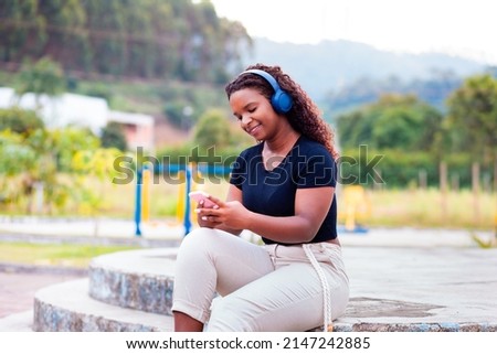 Young happy black woman holding a smartphone.  Using mobile app or social networks on smartphone on the street.