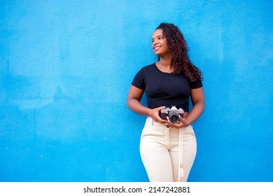 Young happy black woman taking pictures with her camera in front of a blue wall. - Shutterstock ID 2147242881