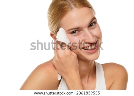 young happy blond woman cleans her face with wet wipes on white background