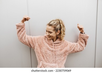 Young happy blonde successful girl stands in front of a metal wall and makes a victory pose with her arms