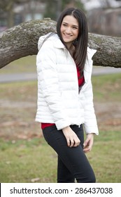 A Young And Happy Brunette Girl Wearing A White Puffy Coat In The Fall On A Cloudy Day.