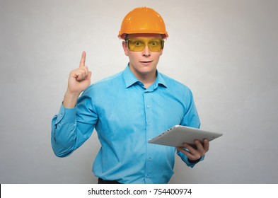 Young Happy Builder Worker In A Hard Hat Holding In Hand A Tablet Computer And Rise His Index Finger Up Isolated. New Idea Concept. The Obvious Solution.