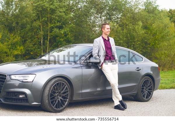 Young happy\
business man in the car. Man in a suits standing by the expensive\
sport car. Successful young man.\
