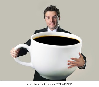 young happy business man holding a funny huge and oversized cup of black coffee in caffeine addiction concept isolated on even background
