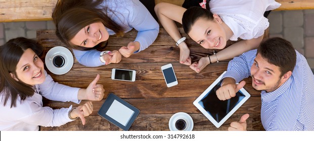 Young Happy Business People From Above Top View of Smiling Business Men At Wooden Desk Looking Smiling with Tablet Computers Telephones Coffee Mug Casual Clothing