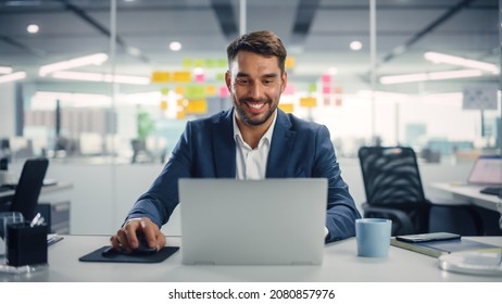 Young Happy Businessman Using Computer in Modern Office with Colleagues. Successful Handsome Manager Smiling, Working on Financial and Marketing Projects. Drinking Tea or Coffee from a Mug. - Powered by Shutterstock