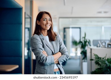 Young happy businesswoman with arms crossed standing int he office and looking at camera. - Shutterstock ID 2345695197