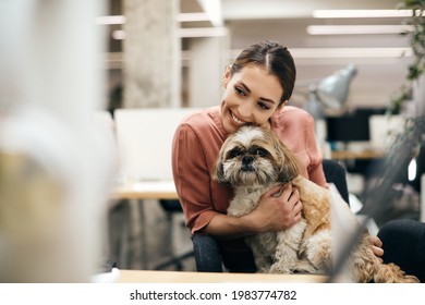 Young happy businesswoman holding her dog while taking a break from work in the office. - Powered by Shutterstock