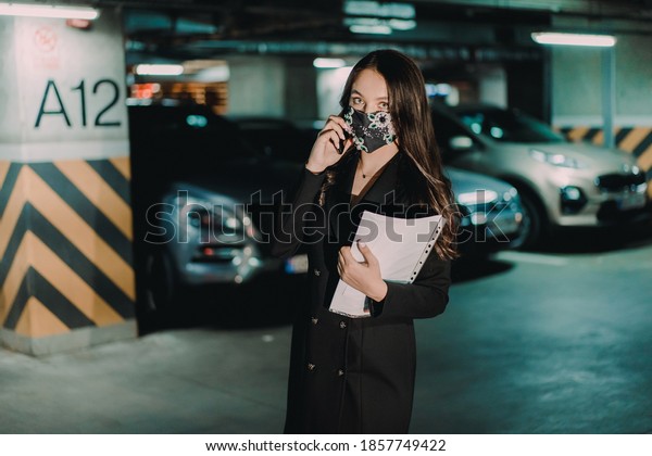 Young happy businesswoman\
with pandemic mask communicating over mobile phone in underground\
parking.