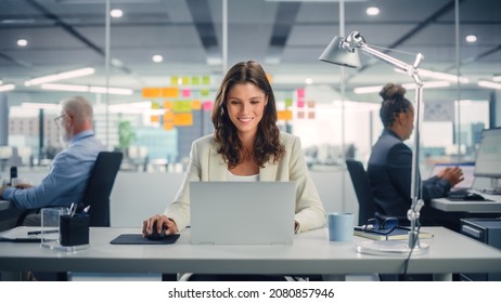 Young Happy Businesswoman Using Computer in Modern Office with Colleagues. Stylish Beautiful Manager Smiling, Working on Financial and Marketing Projects. Drinking Tea or Coffee from a Mug.