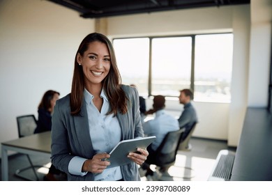 Young happy businesswoman using digital tablet in meeting room and looking at camera. Copy space.