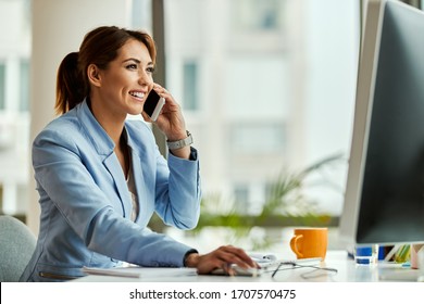 Young happy businesswoman working on desktop PC and communicating over mobile phone in the office.