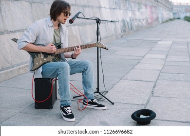 Young happy busker playing guitar and singing at city street