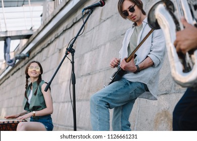 Young Happy Buskers With Guitar, Drum And Saxophone At City Street