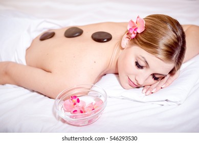 Young happy caucasian blond woman getting a hot stone massage spa procedure and smiling at camera