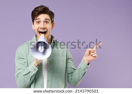 Young happy caucasian man 20s in casual mint shirt white t-shirt scream in megaphone shout point index finger aside on workspace isolated on purple background studio portrait People lifestyle concept.